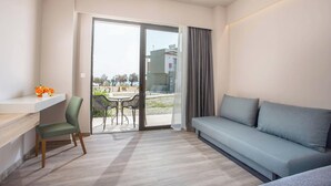 A modern room with a grey sofa, a green chair, a small table with a vase of flowers, and a sliding glass door leading to an outdoor area with a table and chairs. - Gennadi Sea Side Resort (Rhodes)