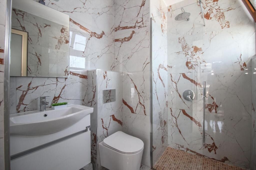 A modern bathroom with a marble sink, toilet, and shower.