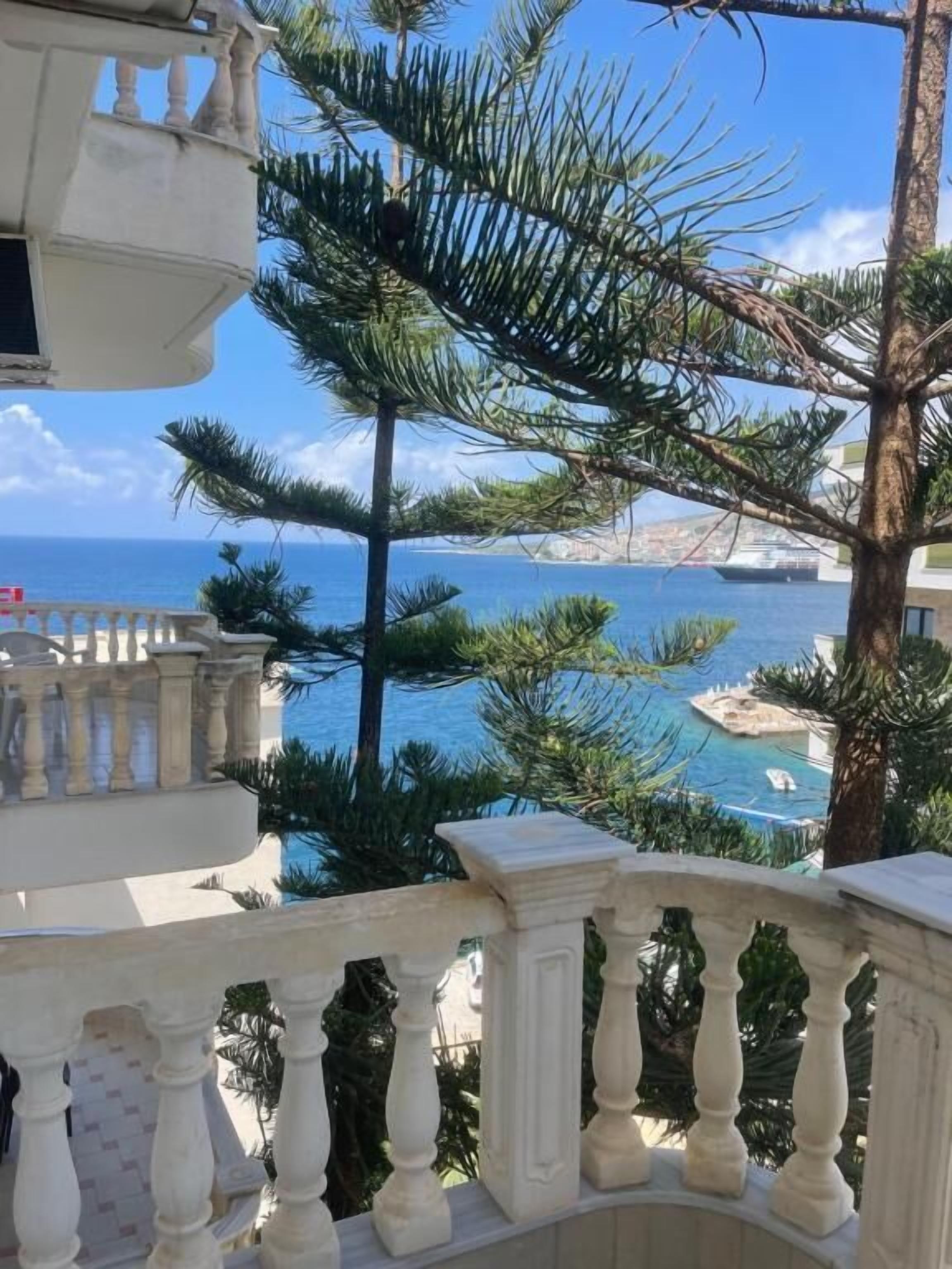 A balcony with a view of the sea and a pool area.