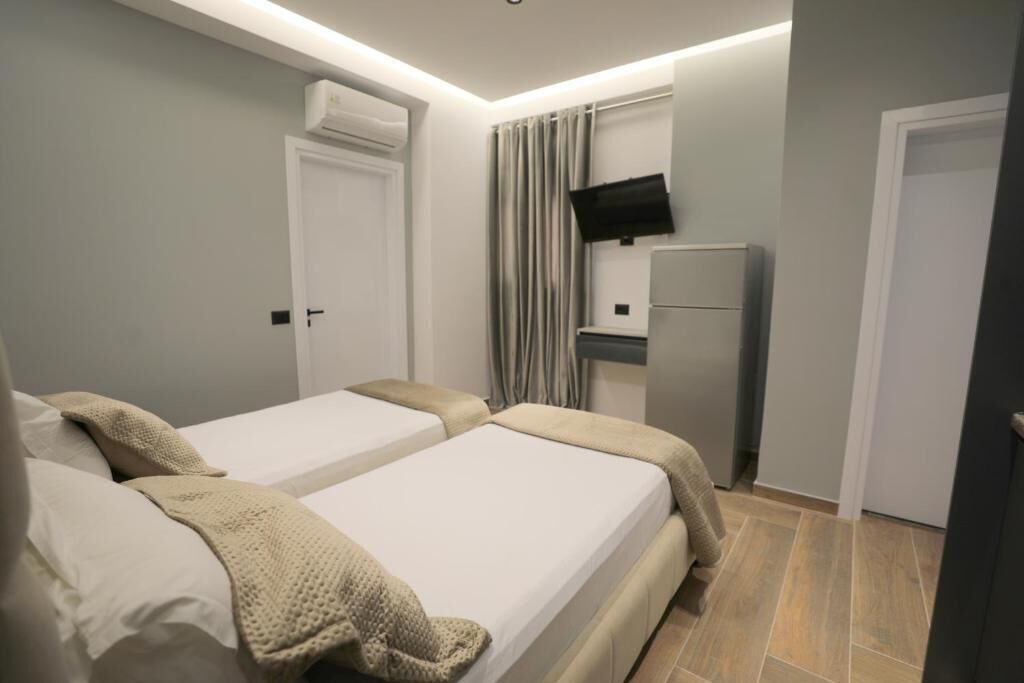 A bedroom with two beds, a TV mounted on the wall, a refrigerator, and a door.