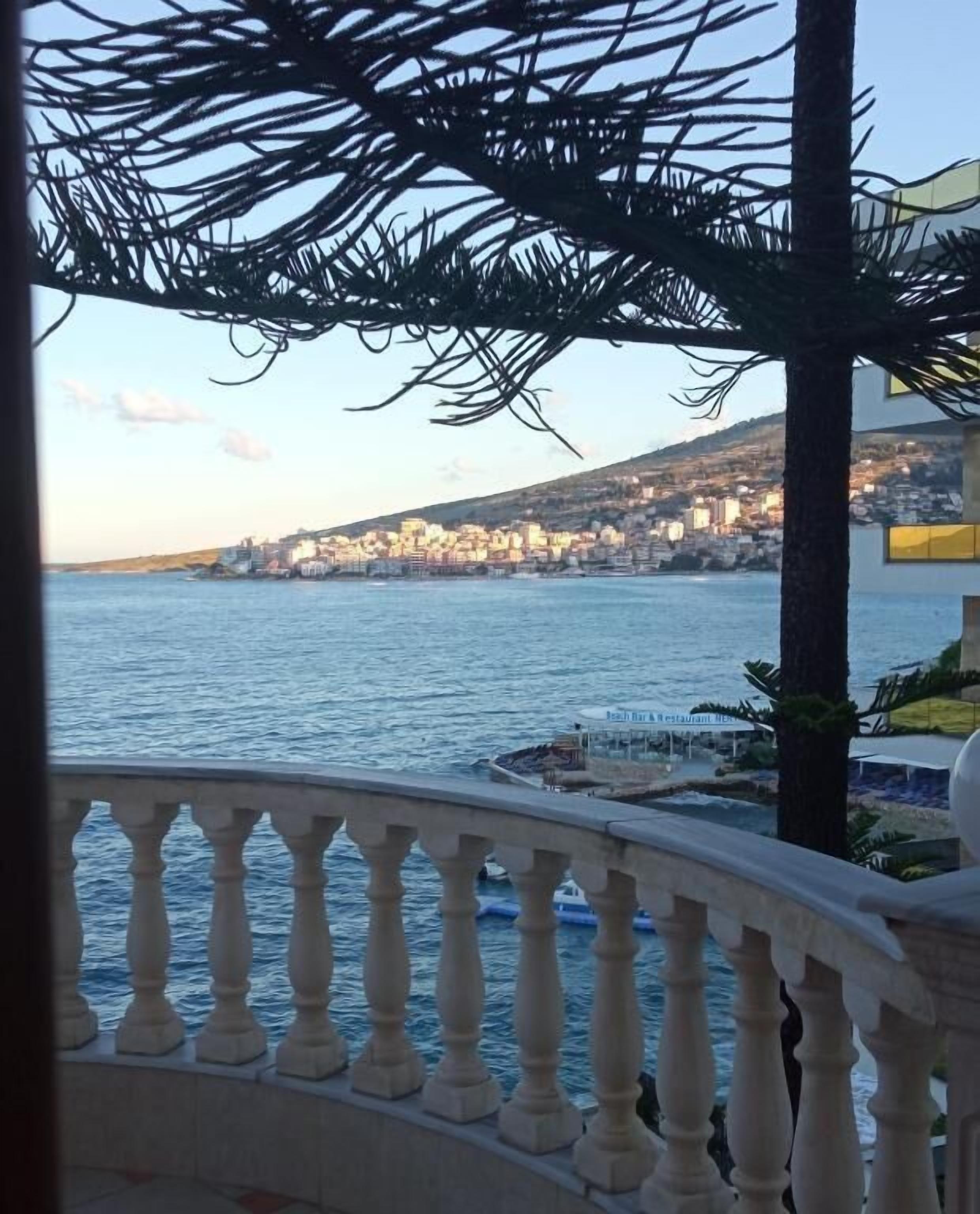 A coastal view from a balcony with a railing, overlooking a beach area with a restaurant named "Beach Bar Restaurant."