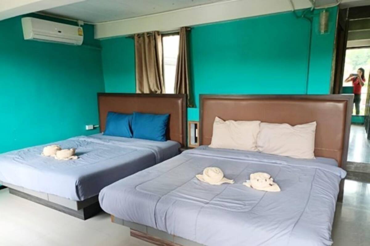Deux lits jumeaux avec du linge de lit gris et des serviettes décoratives, un mur de couleur turquoise et une fenêtre avec des rideaux.
