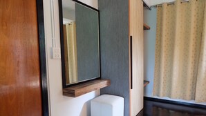 Een moderne badkamer met een grote spiegel, een klein wit bankje en een douchegordijn.