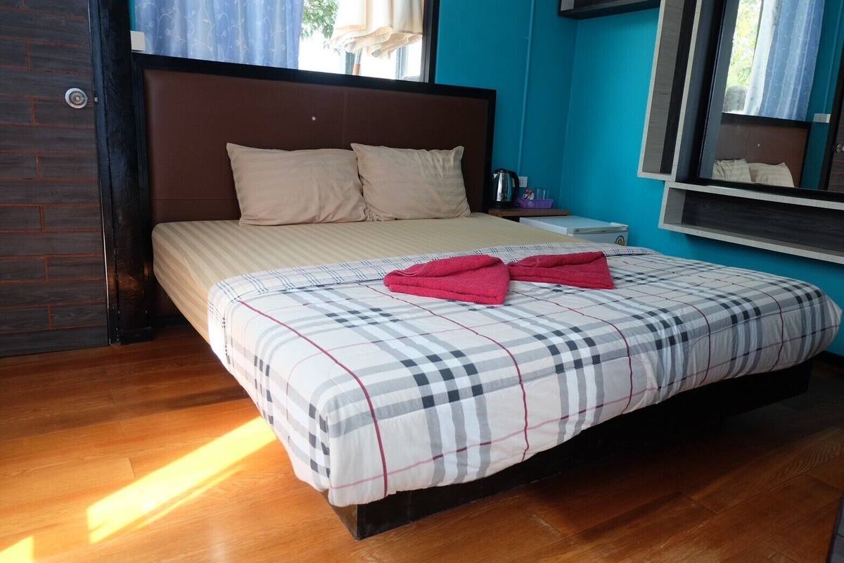 Une chambre à coucher avec un lit, des oreillers, une table de chevet, une fenêtre et une vue sur l’extérieur.