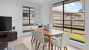Un comedor con mesa, sillas, televisor y vista a un patio trasero con cerca de madera.
