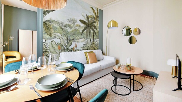 A dining area with a table set for four, a sofa, and a mural of a tropical scene on the wall.
