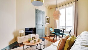 A modern living room with a sofa, a coffee table, a TV, and a dining area with chairs and a table.