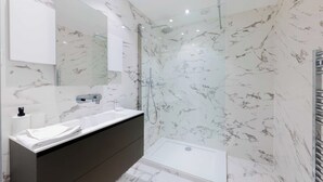 Et moderne badeværelse med marmorbeklædning, en brusekabine med glasvægge og et toiletbord med vask og spejl.