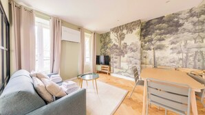 En stue med sofa, et rundt bord, et spisebord med stole og et mural på væggen.