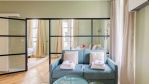Et moderne værelse med en blå sofa, et glasbord og en skydedør til en balkon.