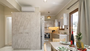 Une cuisine moderne avec des meubles de rangement en marbre, un coin repas avec une table dressée pour deux personnes, et une vue sur l’extérieur.