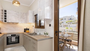 Une cuisine moderne dotée de plans de travail en marbre, d’un four encastré et d’un coin repas avec un balcon donnant sur un quartier résidentiel.