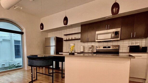 A modern kitchen with a large island, dark wooden cabinets, and a view through a large window. - A historic 700 square foot Atrium loft in the heart of the Old Market (Omaha)