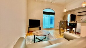 A modern living room with a sofa, a coffee table, a TV, and a kitchen area with a fridge and cabinets. - A historic 700 square foot Atrium loft in the heart of the Old Market (Omaha)