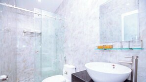 A modern bathroom with a glass shower enclosure, a white toilet, a large white sink with a glass shelf above it, and a mirror. - Moonlight Quynhon Hotel (Quy Nhon Nam)