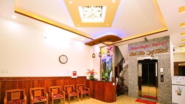 A hotel reception area with a wooden reception desk, several chairs, a clock, and a sign for the Moonlight Hotel. - Moonlight Quynhon Hotel (Quy Nhon Nam)