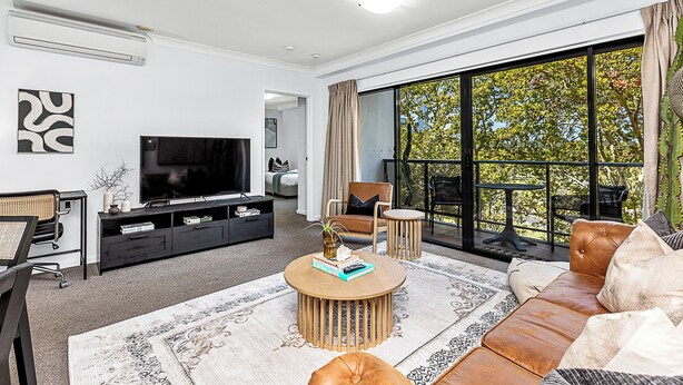 A modern living room with a flat-screen TV, a sofa, a coffee table, and a large window offering a view of trees. - Luxury Perth Getaway: Modern Design (Perth WA)