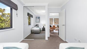 A modern hotel room with a large window, a bed, a desk, and a seating area with a sofa and a coffee table.