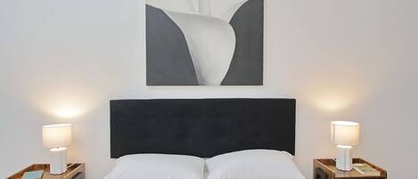 Una habitación de hotel con una cama grande, dos mesitas de noche con lámparas y una obra de arte colgada en la pared.