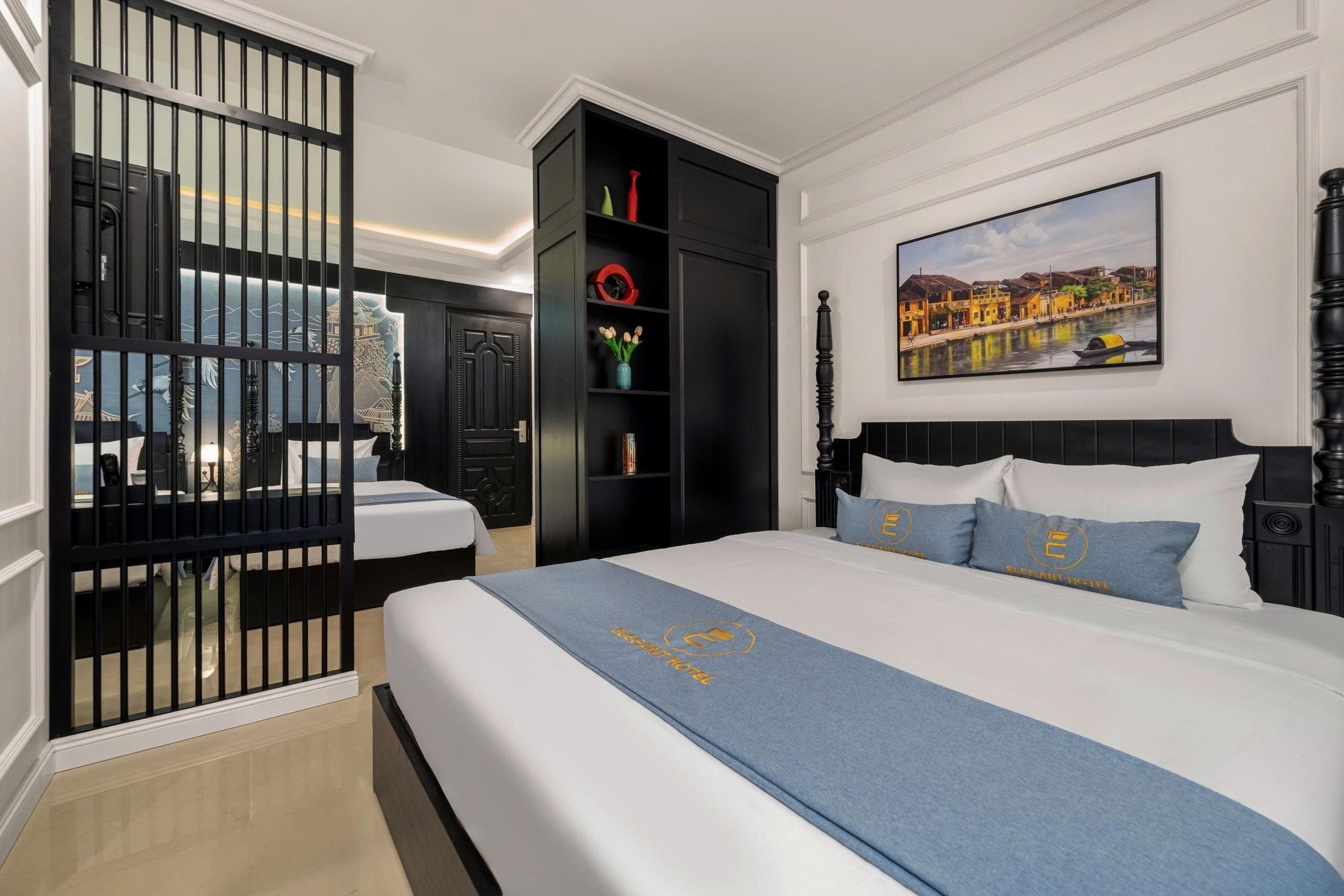 A hotel room with a large bed, a black wardrobe, a painting on the wall, and a view of the cityscape through a window.