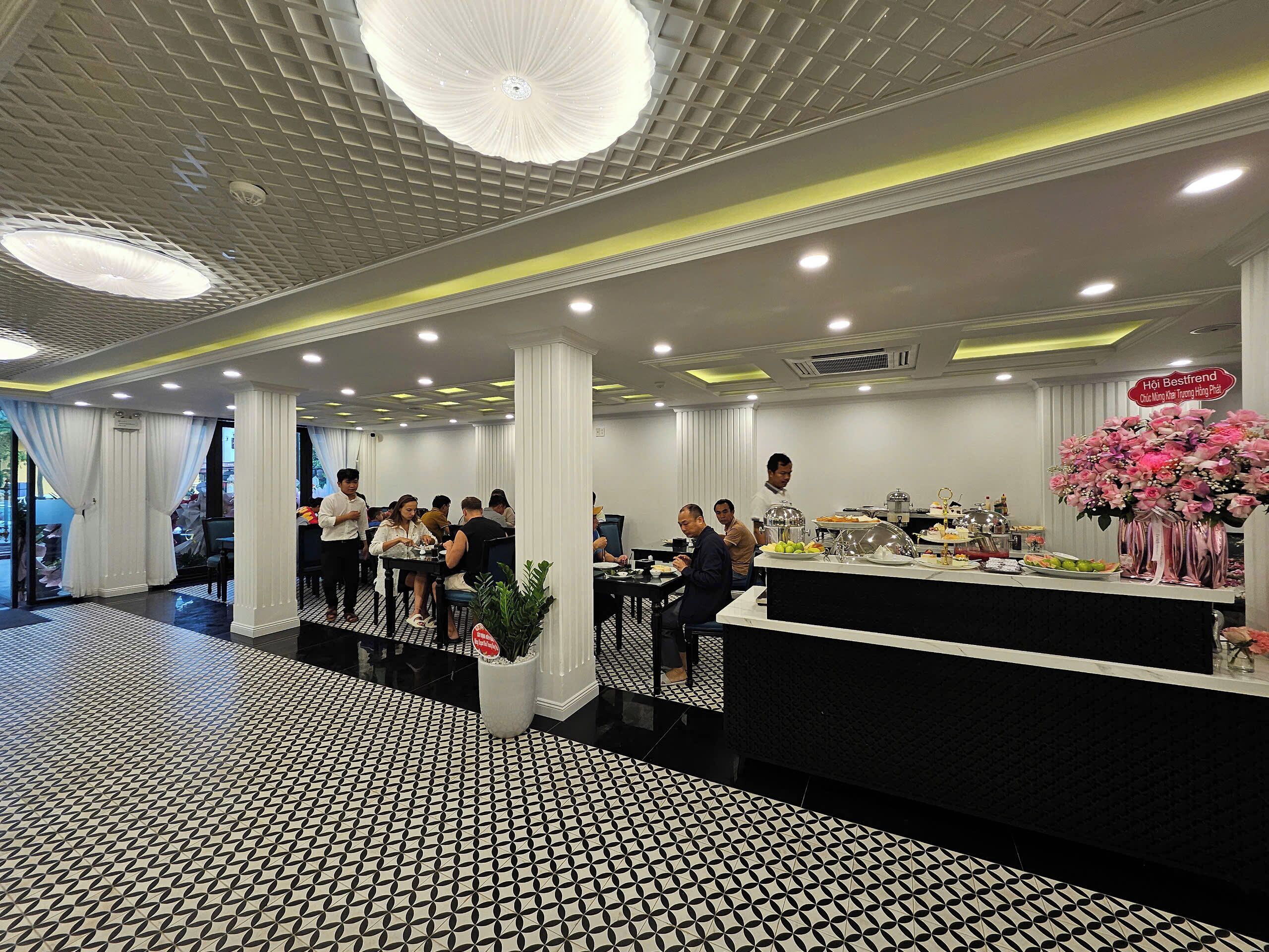 A restaurant with a black and white patterned floor, white pillars, and a central counter with food and drinks.