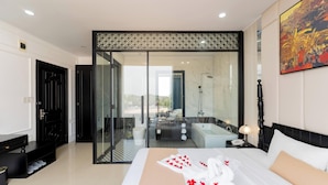 A modern hotel room with a large bed, a glass shower enclosure, a bathtub, and a view through the glass door. - Elegant Hotel (Hue)