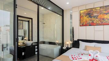 Habitación de hotel moderna con cabina de ducha de vidrio, una cama grande con toalla decorativa, una mesita de noche con lámpara y un cuadro abstracto de grandes dimensiones en la pared.