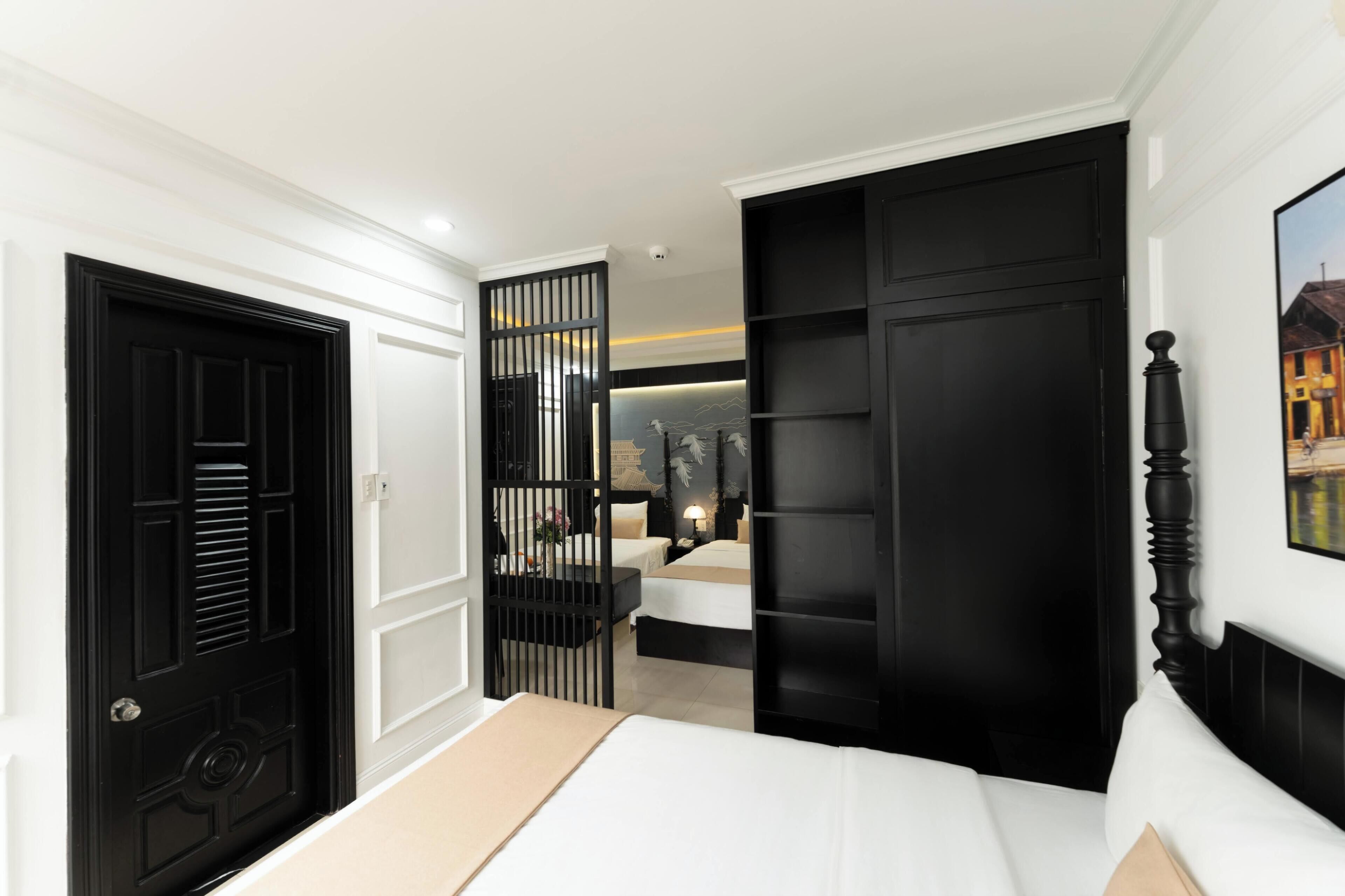Un dormitorio con una cama, un armario negro, una puerta blanca y una estantería de pared.