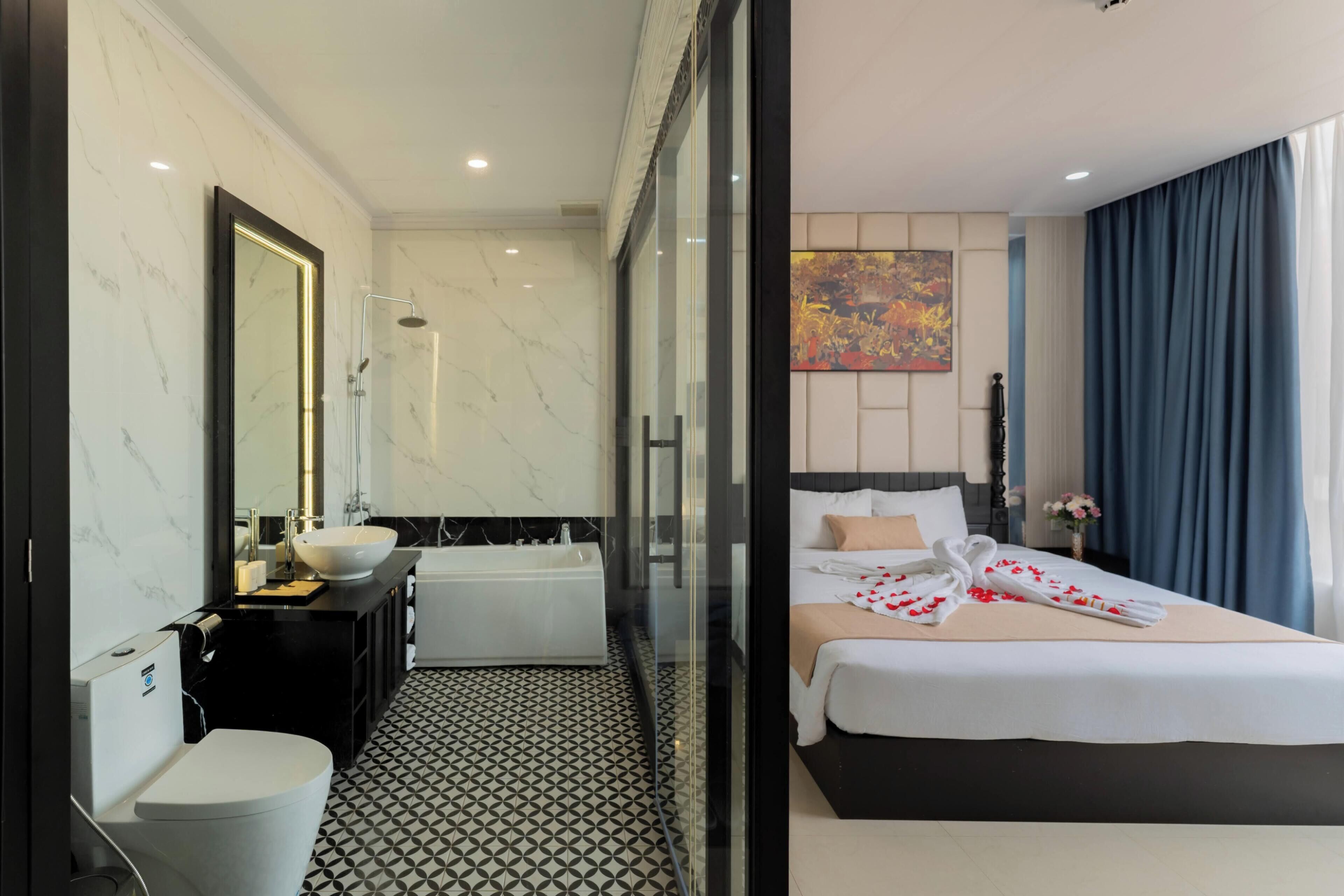 A hotel room with a bathroom, a bed, a large mirror, and a painting on the wall.