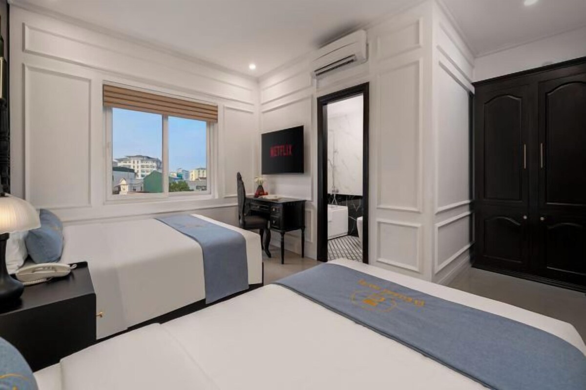 A hotel room with two beds, a desk, a TV, and a wardrobe.