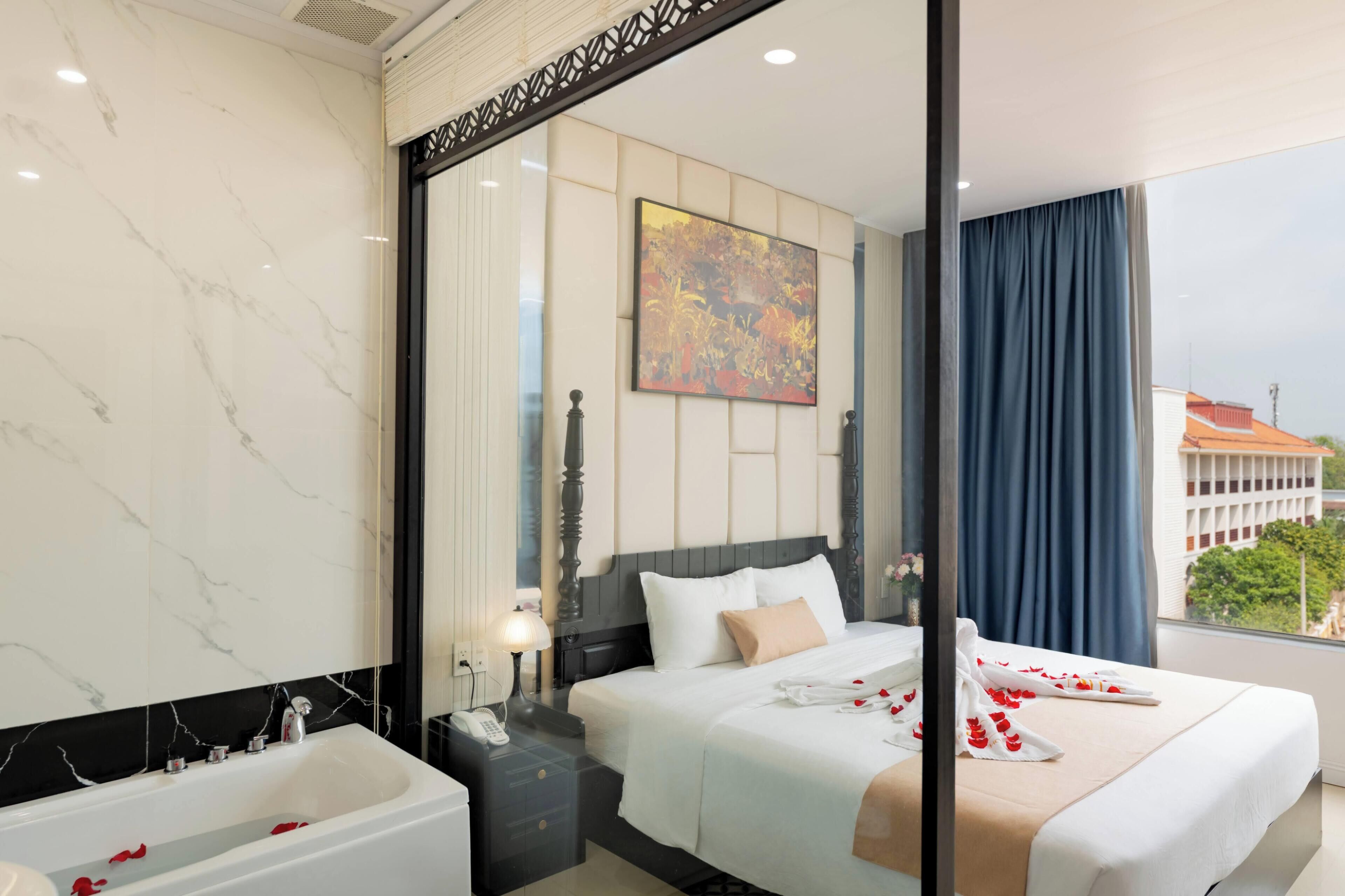 Habitación de hotel con una cama grande, una bañera, una mesita de noche con lámpara y un cuadro en la pared.