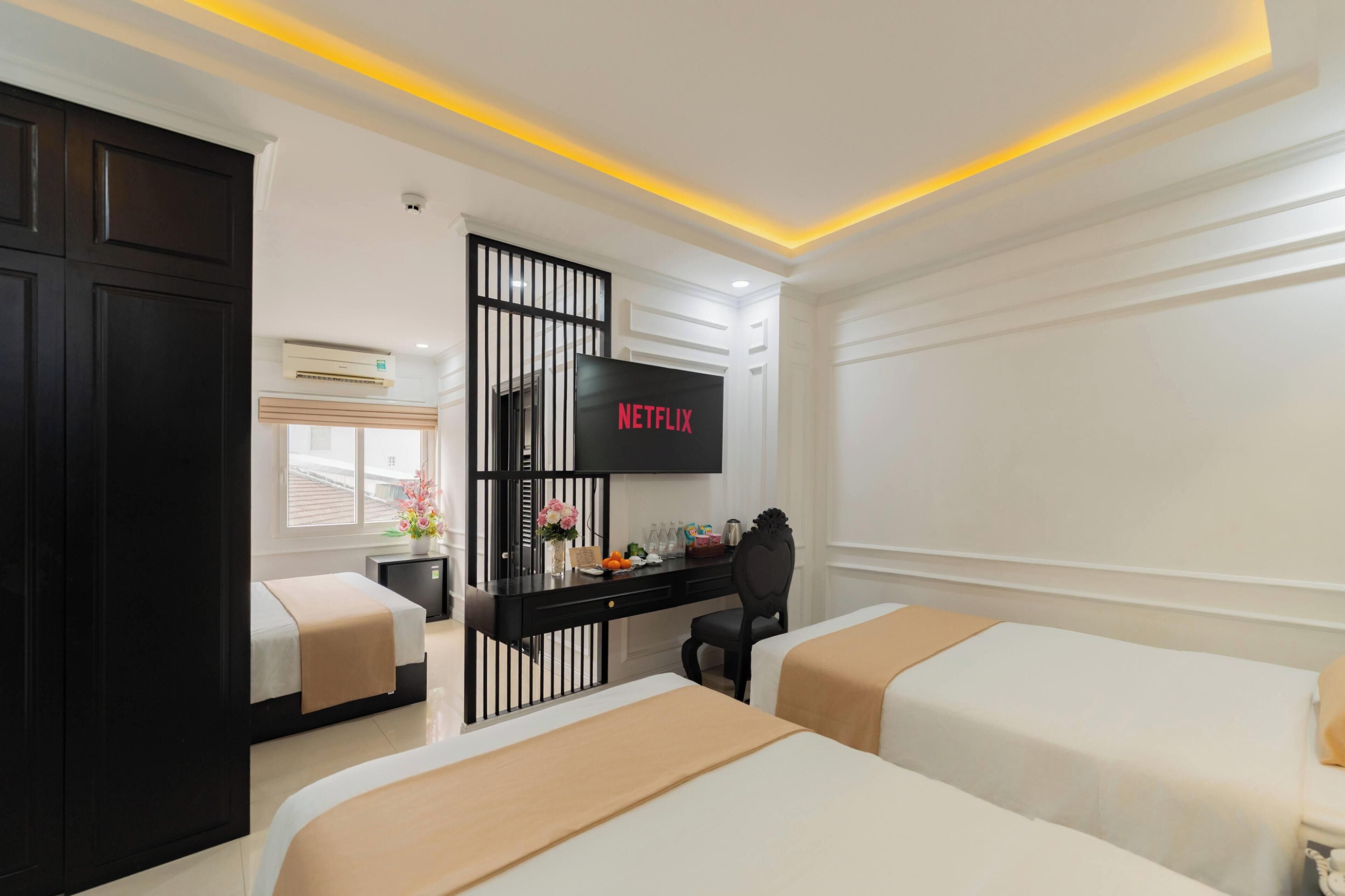 Une chambre d’hôtel avec deux lits, un bureau avec une télévision et une fenêtre avec des stores.
