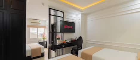 Une chambre d’hôtel avec deux lits, un bureau avec une télévision et une fenêtre avec des stores.