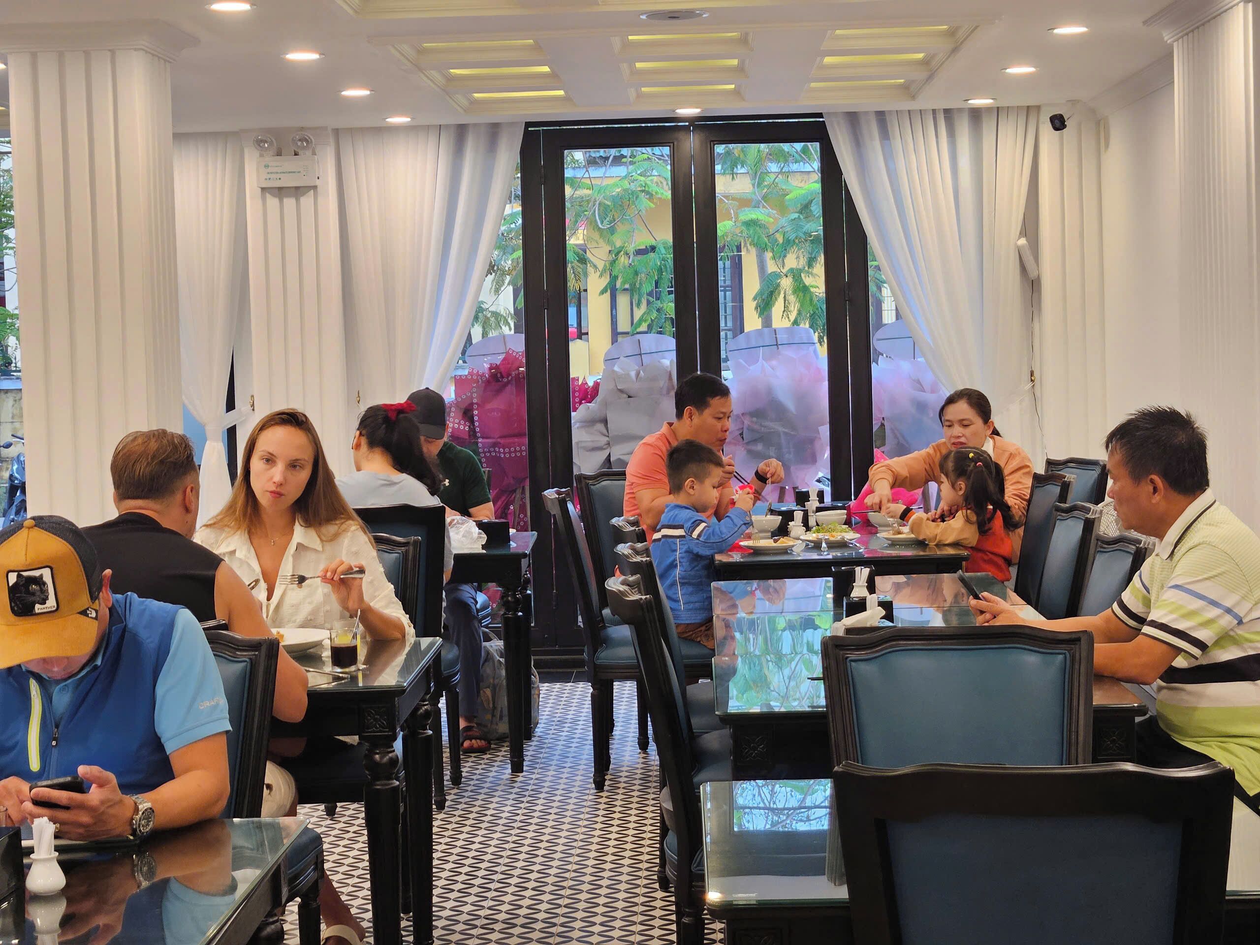 Un restaurante con una decoración moderna, mesas y sillas de vidrio, y vistas al exterior con zonas verdes.