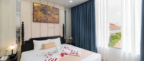 Habitación de hotel con una cama grande, una mesita de noche con lámpara, un cuadro en la pared y vistas al exterior a través de la ventana.