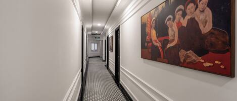 A hallway with a patterned floor, a painting on the wall, and doors leading to rooms.