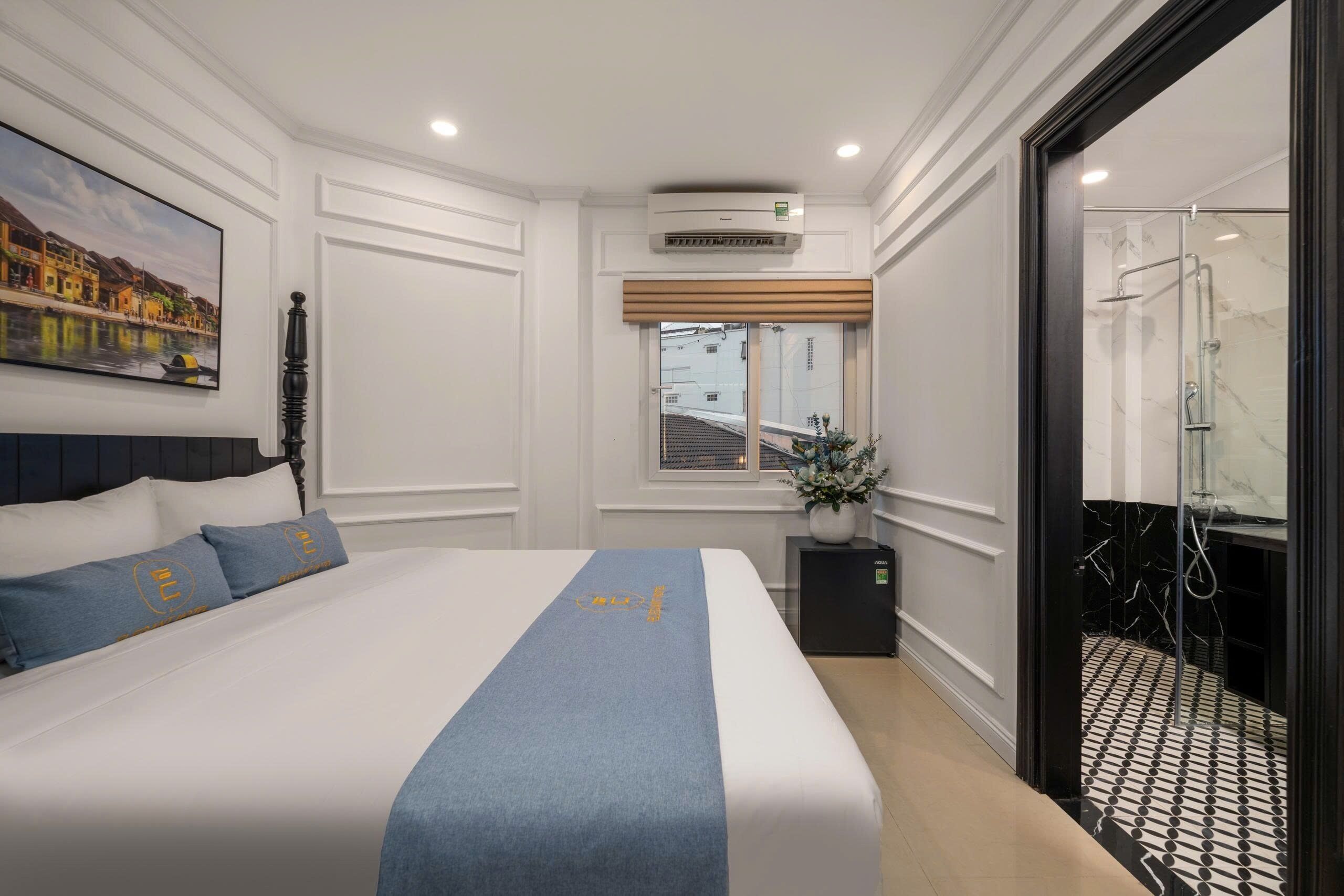 A hotel room with a bed, a window with a view, an air conditioning unit, and a shower area.