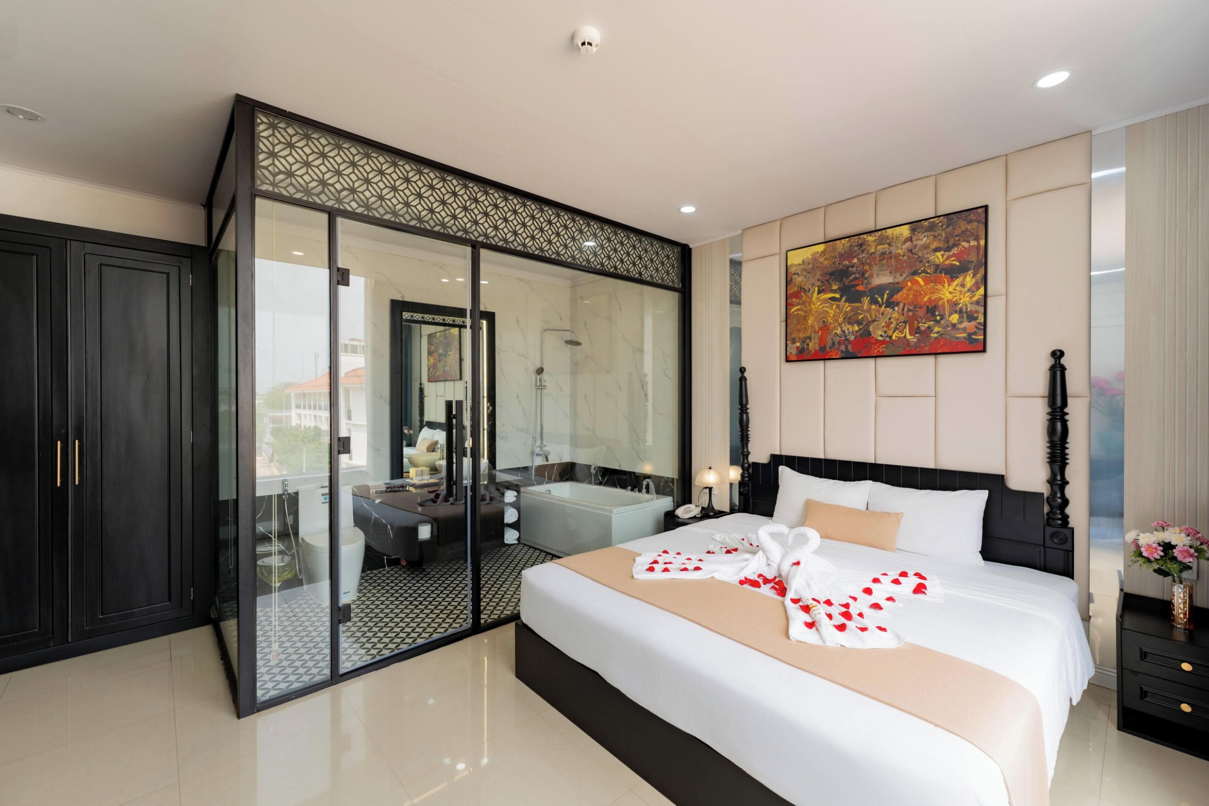A modern hotel room with a large bed, a glass-enclosed walk-in closet, a bathtub, and a large painting on the wall.