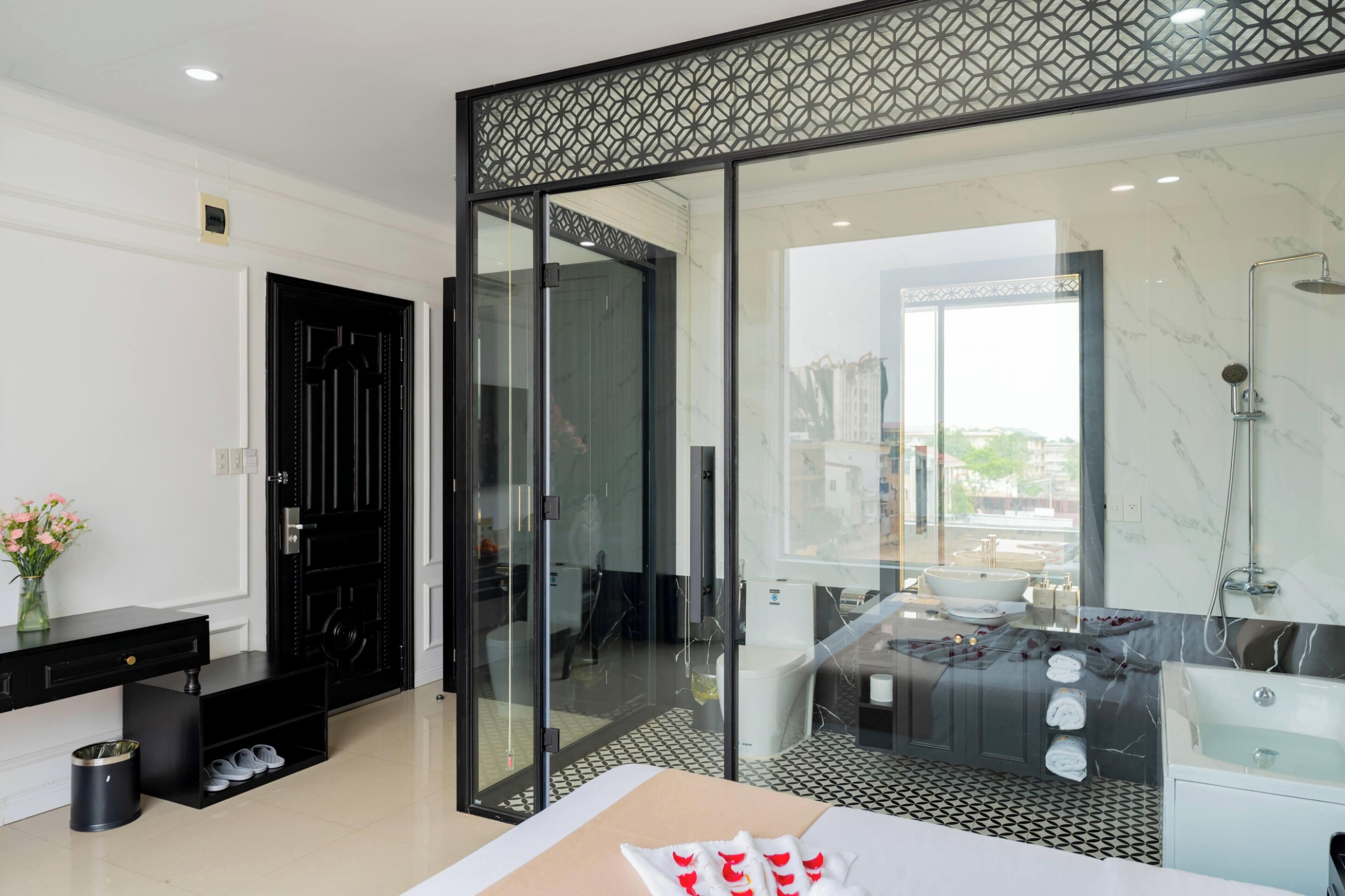 A modern hotel room with a glass partition, a black-framed door, a bathroom with a bathtub, and a tiled floor.