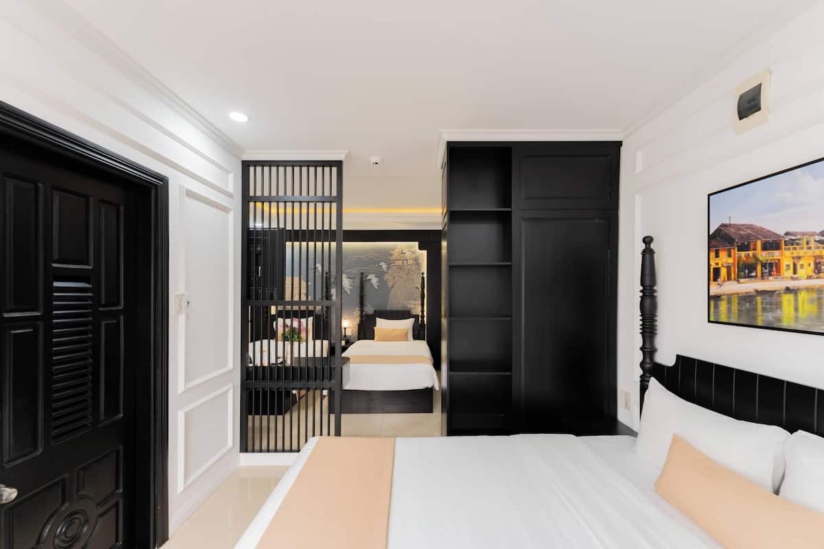 A bedroom with a bed, a black wardrobe, a black door, and a painting on the wall.