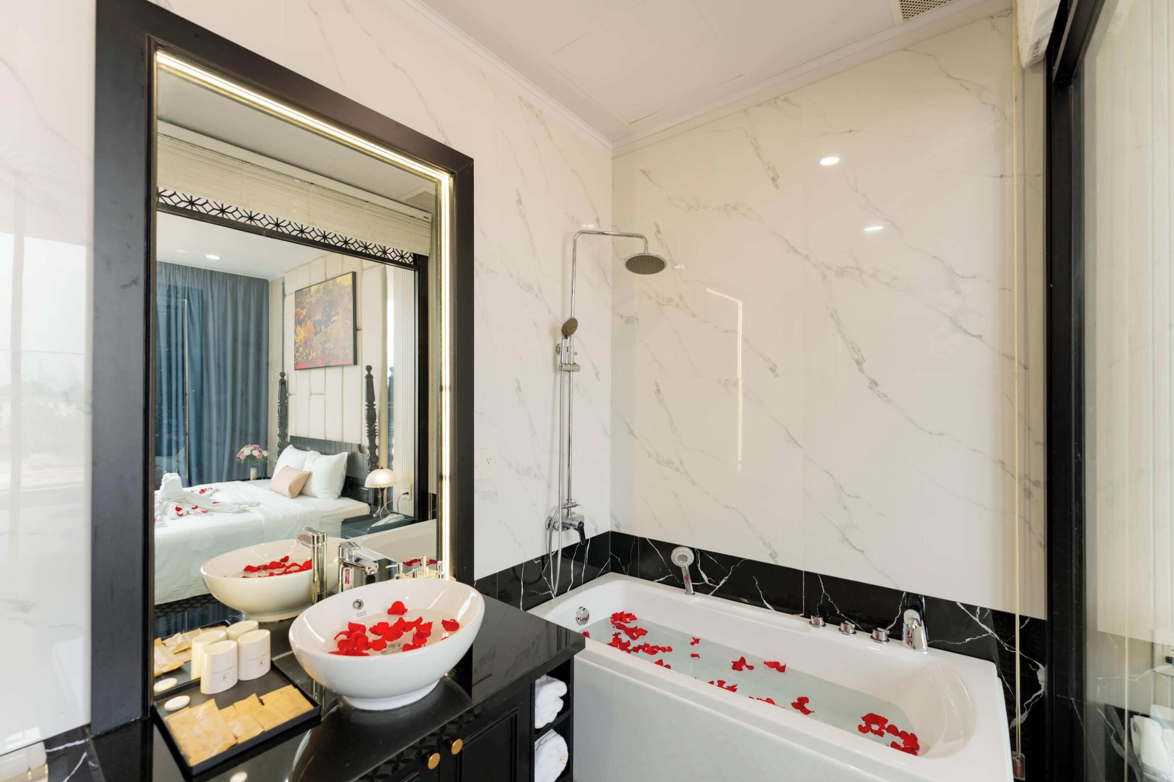 A bathroom with a large mirror, a white bathtub with rose petals, a white sink, and a shower.