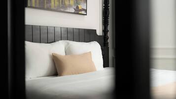 Una cama con ropa blanca y una sola almohada color beige, cabecera de madera oscura, y un cuadro con una vista de un canal arriba.