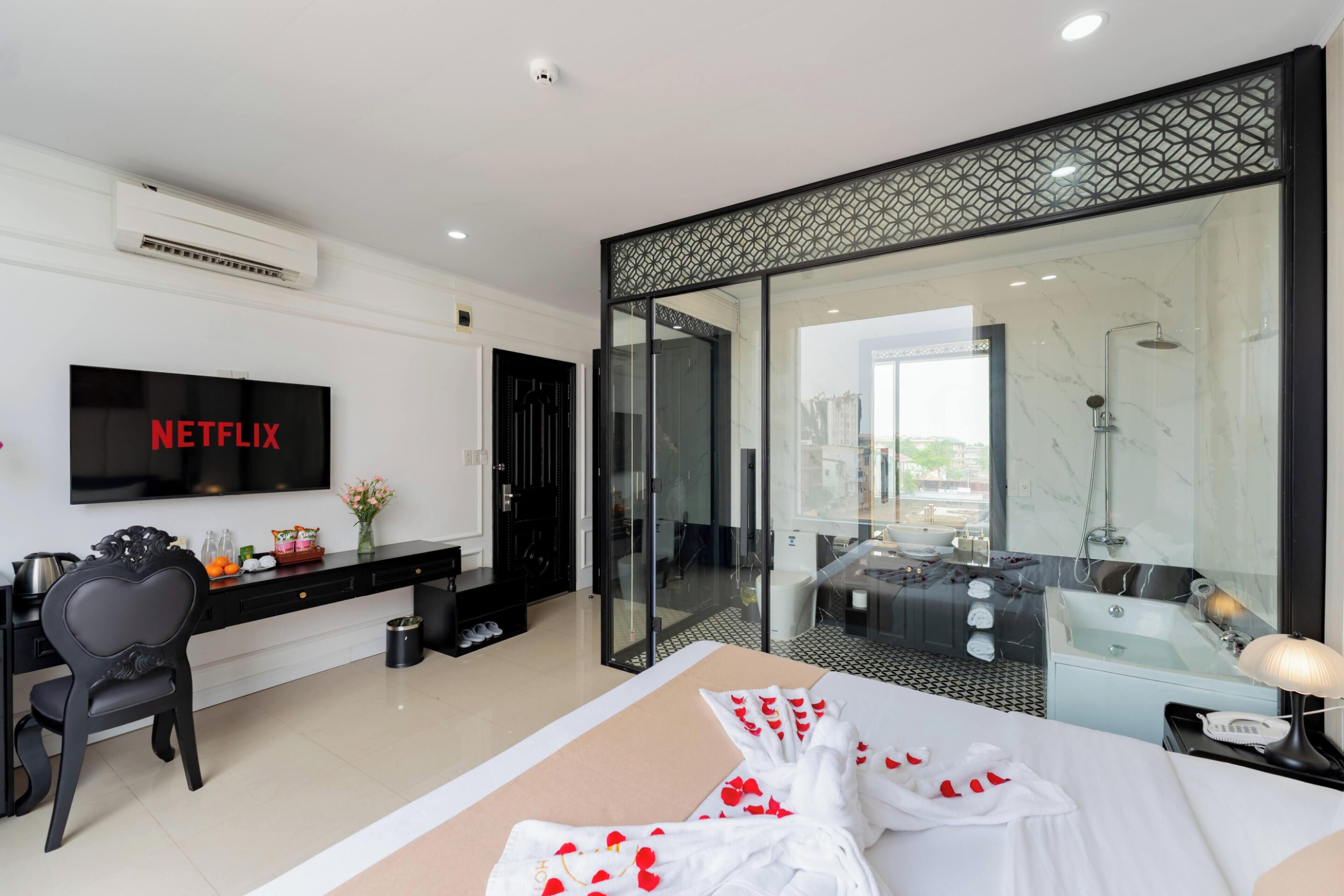 Una habitación de hotel moderna con una cama grande, televisión, escritorio y baño con bañera y ducha.