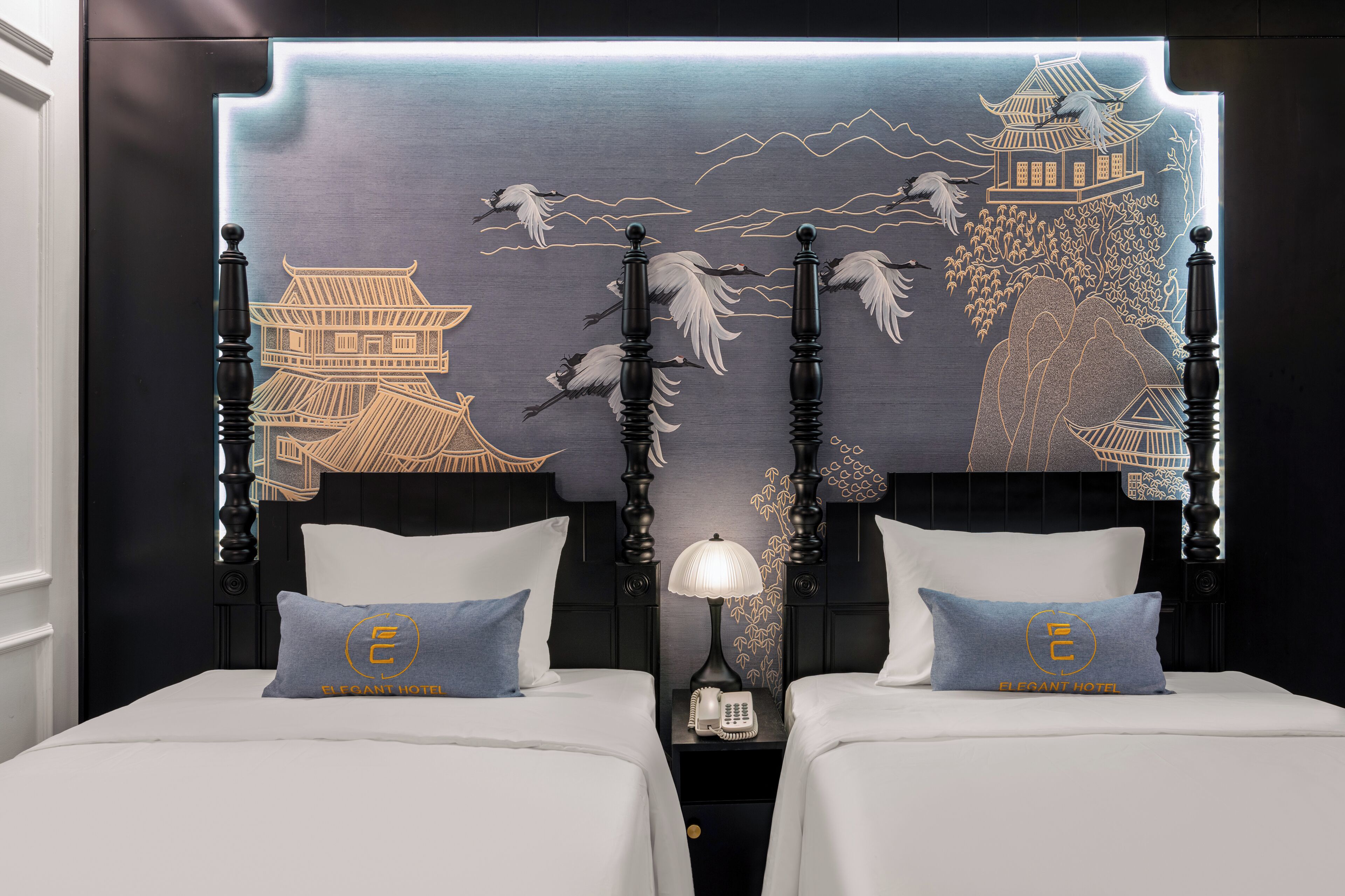A hotel room with two beds, a nightstand with a lamp, and a wall mural depicting traditional architecture.