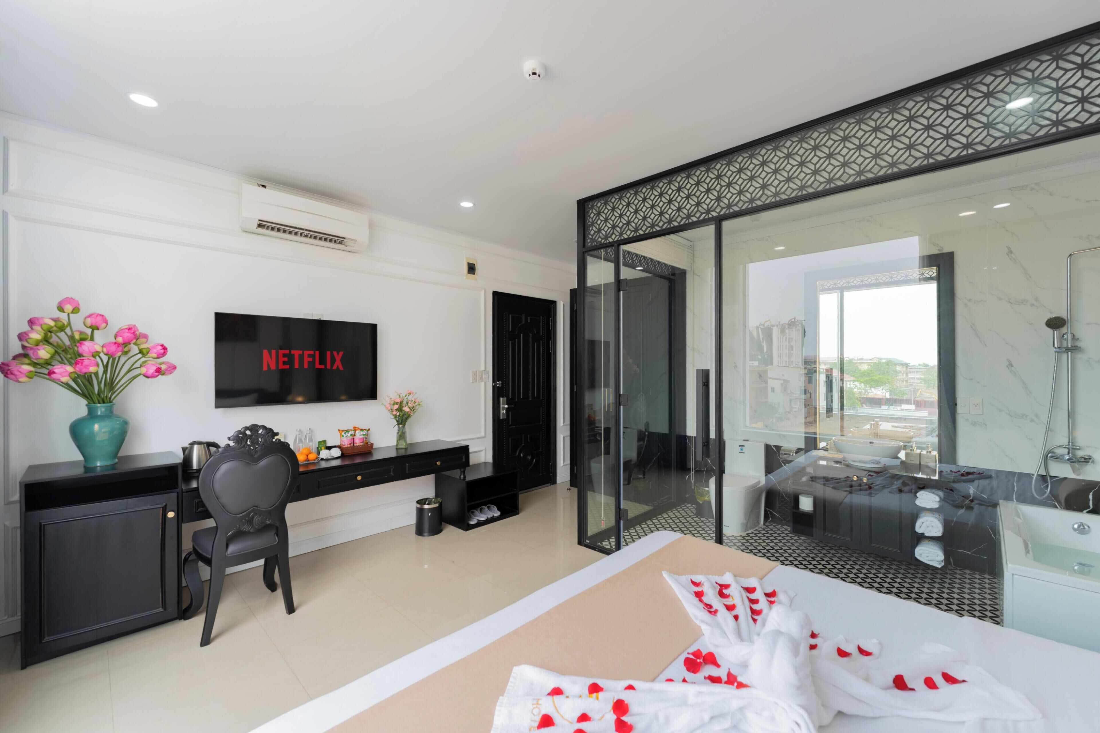 Une chambre d’hôtel moderne équipée d’un lit, d’un bureau avec un ordinateur, d’une télévision et d’une salle de bain avec une douche en verre, le tout offrant une vue sur la ville.