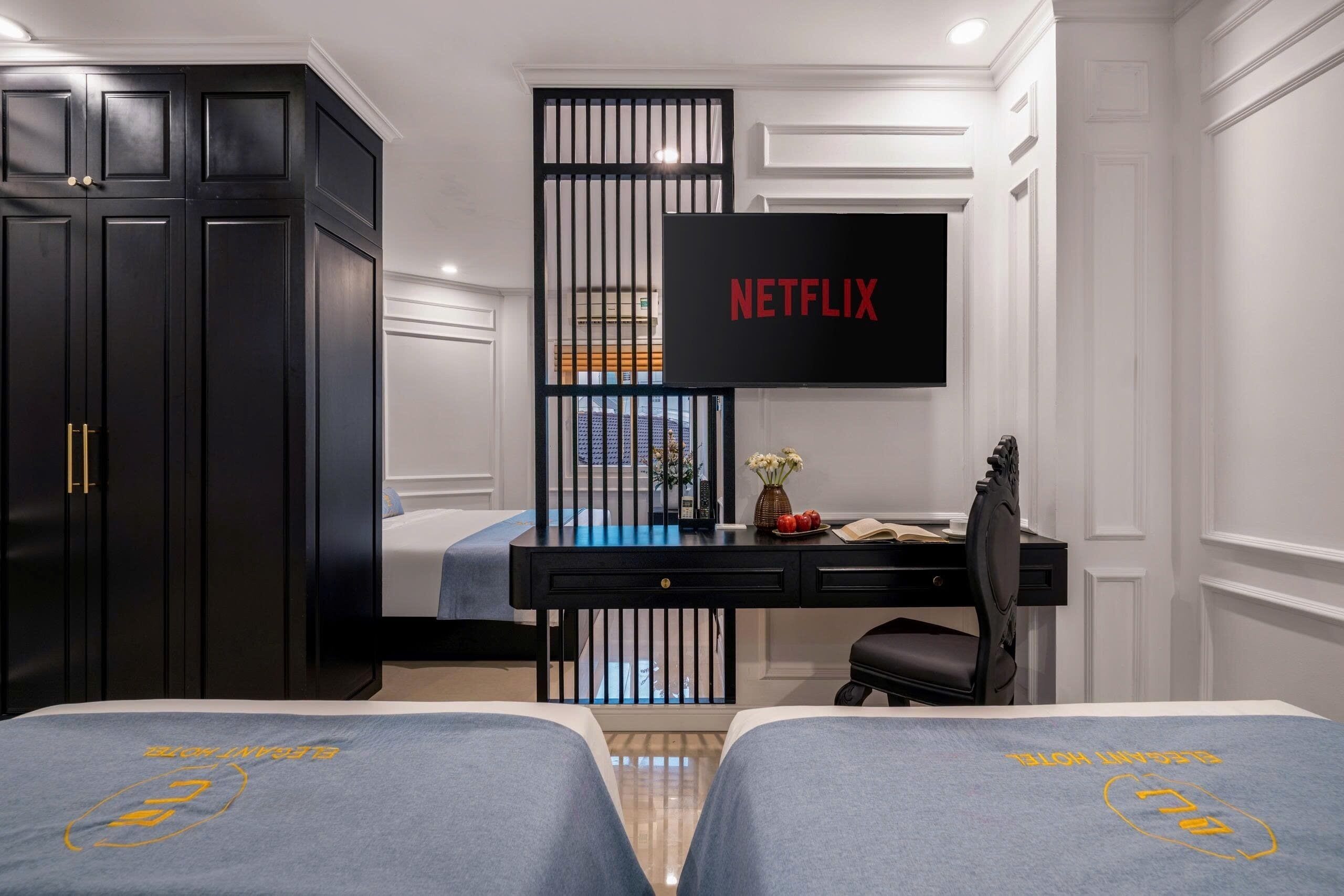A bedroom with a bed, a desk with a computer, a TV mounted on the wall, and a wardrobe.