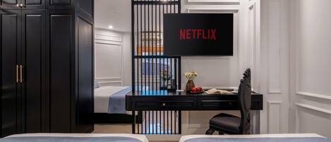 A bedroom with a bed, a desk with a computer, a TV mounted on the wall, and a wardrobe.