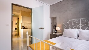 A hotel room with a bed, a bedside table with a lamp, a small potted plant, and a view of the kitchen area. - Family home w. yard in Beating Heart of Old Town (Chania)