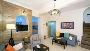 A modern living room with a flat-screen TV, a sofa, a coffee table, and a staircase. - Family home w. yard in Beating Heart of Old Town (Chania)