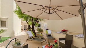 An outdoor patio with wicker furniture, a large umbrella, and potted plants. - Family home w. yard in Beating Heart of Old Town (Chania)
